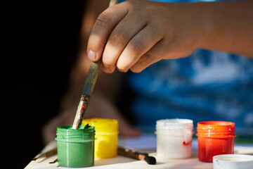 A child's hand with a brush draws gouache paint.