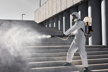 cleaning, disinfection of the city. professional worker man in white protective suit cleans the stairs with spray, sanitation and disinfection service - obrazy, fototapety, plakaty