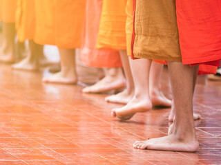 Close up feet of Bhuddist monks in orange rope walking barefoot in the temple to get food offerings