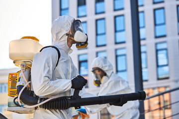 side view on young hard-working male in protective suit with big equipment in hands, going to...