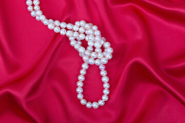 Natural pearls beads tied in a knot on a bright red silk background.Pearl necklace.Close up.Selective focus.Сoncept of valuable Jewelry romantic gifts.