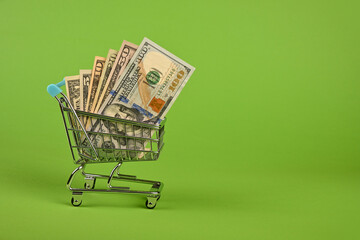 US dollar banknotes in shopping cart over green
