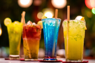 Cold multicolour alcoholic beverages in an exotic restaurant garnished with lemon piece and ecofriendly wooden straw with bokeh
