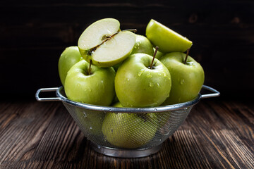 washed fresh juicy green apples in a metal colander on a dark wooden background