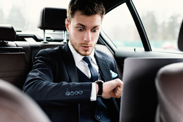 Young businessman looking at wrist watch in his car