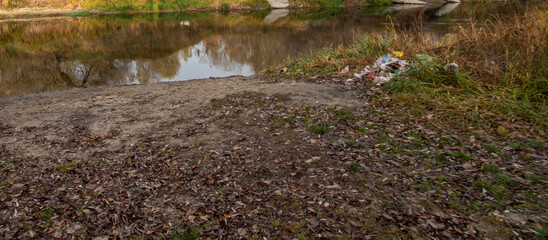 River bank with pile of plastic bottles, dead leaves and orange reed. Example of pollution environment by human activities. Natural background, horizontal orientation picture, copy space.