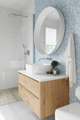 Corner of hotel bathroom with white and blue tiled walls, large white mirror and a shower....