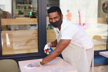 black man waiter wiping table in street cafe, pleasant staff prepare table for clients