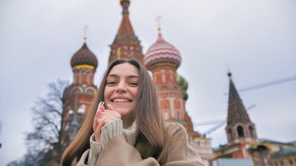 Fototapeta premium Happy smiling young woman portrait in Red Square, Moscow. A woman in the city warms her hands.