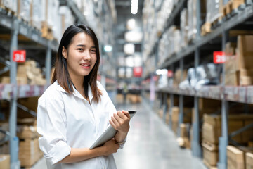 Portrait of Asian young woman enjoying and smile doing checking stock of products in warehouse by using a tablet checking inventory levels , Logistics concept.