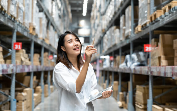 Portrait of Asian young woman enjoying doing checking stock of products in warehouse by using a tablet checking inventory levels , Logistics concept.