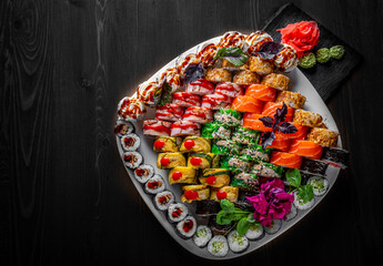 set of sushi roll with salmon, avocado, cream cheese, cucumber, rice, caviar, eel, tuna in plate on black wooden table background