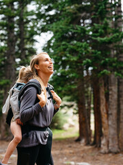 Mom carrying daughter on her back through the woods while hiking in Colorado