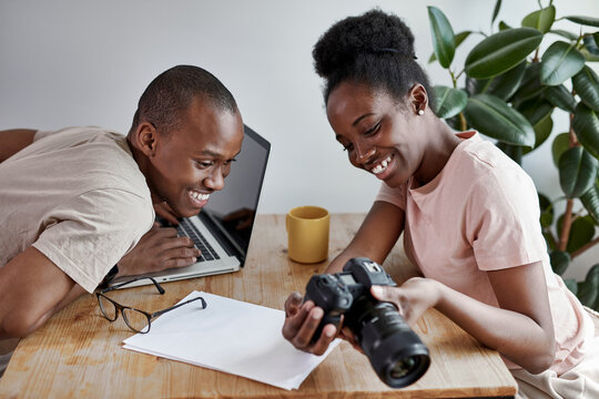 charming african woman shows photos on camera to husband, man look and they smile. work at home, freelance