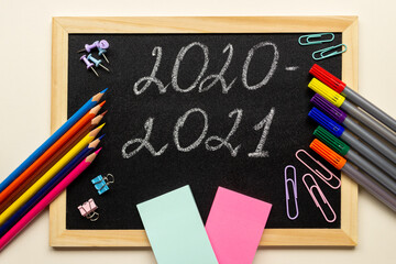 Blackboard with various stationery: pencils, felt-tip pens, paper clips and stickers. Lettering 2020-2021. Back to school and new academic year concept.