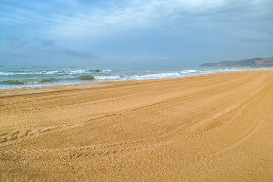 Gava Playa beach in Castelldefels, Barcelona, Spain. Bright seashore cleaned of debris and tyre tracks. Big waves, mountains in the background. Morning in nature