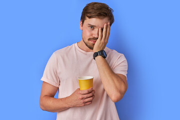 Fototapeta premium tired guy with cup of coffee, he tries to wake up, freshen up with coffee. isolated blue background