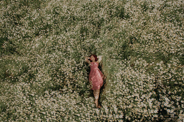 A girl in a red dress lies in a field of daisies.