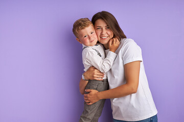 portrait of sweet caucasian child boy with mother isolated over purple background. young mom and kid hugging