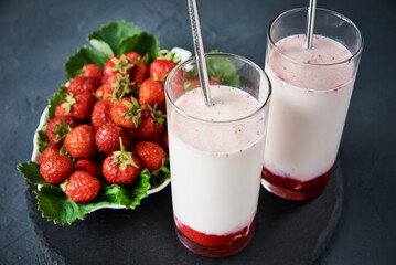 Strawberry milk smoothie in glass with straw on a dark background