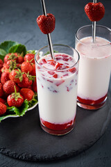 Strawberry milk smoothie in glass with straw on a dark background
