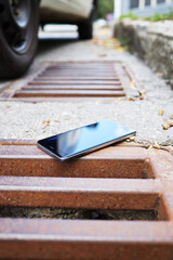 Fototapeta na wymiar lost smart phone device laying on the ground near rain drain at city street.