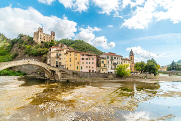 View across the Nevia River of the Saint Anthony Church, arched bridge and the medieval Castle fortress overlooking the Ligurian city of Dolceacqua, Italy,