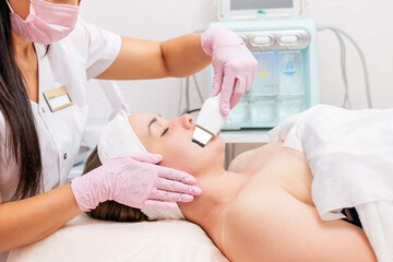 Beauty salon. A cosmetologist wearing a medical mask and rubber gloves cleans the face using an...