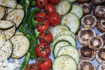 Mix of vegetables on baking paper for grilling. On the plate are tomatoes, eggplant, zucchini, peppers, garlic and mushrooms sprinkled with basil and salt.