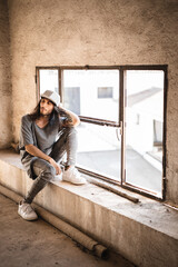 Modelo con pelo largo, ropa gris, gorra gris de visera plana, zapatillas blancas y barba posa...