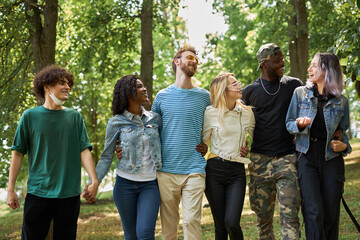 american mixed race youth spend time together in the park, friendly men and women have fun, laugh. international love, friendship, tolerance concept