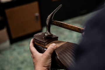 Male cobbler holding shoe and nailing a heel with hummer. Close-up on hands of professional shoemaker.