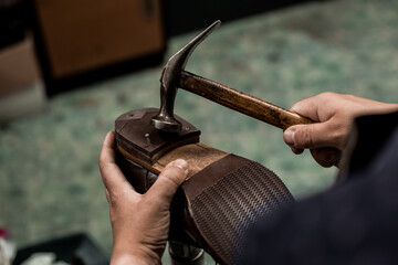 Male cobbler holding shoe and nailing a heel with hummer. Close-up on hands of professional shoemaker.
