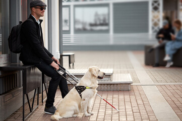 disabled person sit having rest with dog guide outdoors, blind male in safety with his best friend...