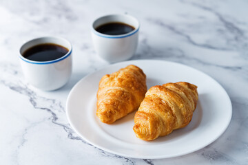 Fresh croissants on a plate with cups of coffee