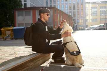 young blind man stroking guide dog in the street, caring favorite pet, best friend. outdoors