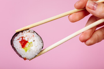 Tasty sushi roll maki with wooden chopsticks on pink background close up. Place for caption and text
