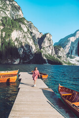woman walking by mountain lake pier with wooden boats in red dress