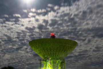 radio telescope illuminated above the night sky and full moon