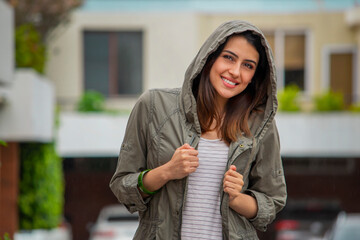 girl in street enjoying the rain and smiling while covering herself with a rain coat / chica se cubre con un abrigo capa mientras disfruta de la lluvia y sonríe
