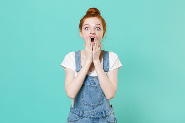 Shocked young readhead girl in casual denim clothes posing isolated on blue turquoise wall...