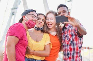 Multiracial friends taking selfie with face mask in coronavirus time - Young people having fun in holiday - new lifestyle concept