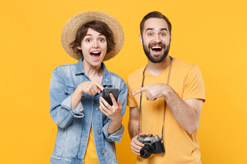 Amazed young tourists couple friends guy girl with photo camera isolated on yellow background....