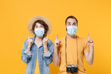 Fototapeta na wymiar Cheerful young tourists couple friends guy girl in sterile face mask isolated on yellow background. Epidemic pandemic coronavirus 2019-ncov sars covid-19 flu virus concept. Pointing index fingers up.