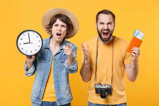 Angry Tourists Couple Friends Guy Girl In Summer Clothes Hat Isolated On Yellow Background. Passenger Traveling Abroad On Weekend. Air Flight Journey Concept. Hold Passport Clock Screaming Swearing.
