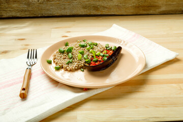 Green buckwheat with baked eggplant with tomato and garlic on a plate on a linen napkin.