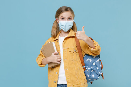 Little kid schoolgirl 12-13 years old in sterile face mask backpack isolated on blue background. Epidemic pandemic coronavirus 2019-ncov sars covid-19 flu virus concept. Hold books showing thumb up.