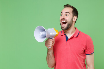 Shocked young bearded man guy in casual red pink t-shirt posing isolated on green background studio portrait. People sincere emotions lifestyle concept. Mock up copy space. Screaming in megaphone.