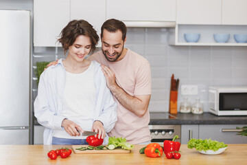 Obraz na płótnie Canvas Cheerful young couple two friends guy girl in casual clothes preparing vegetable salad cooking food in light kitchen at home. Dieting family healthy lifestyle concept. Mock up copy space. Hugging.