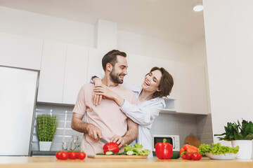 Laughing young couple two friends guy girl in casual clothes preparing vegetable salad cooking food in light kitchen at home. Dieting family healthy lifestyle concept. Mock up copy space. Hugging.